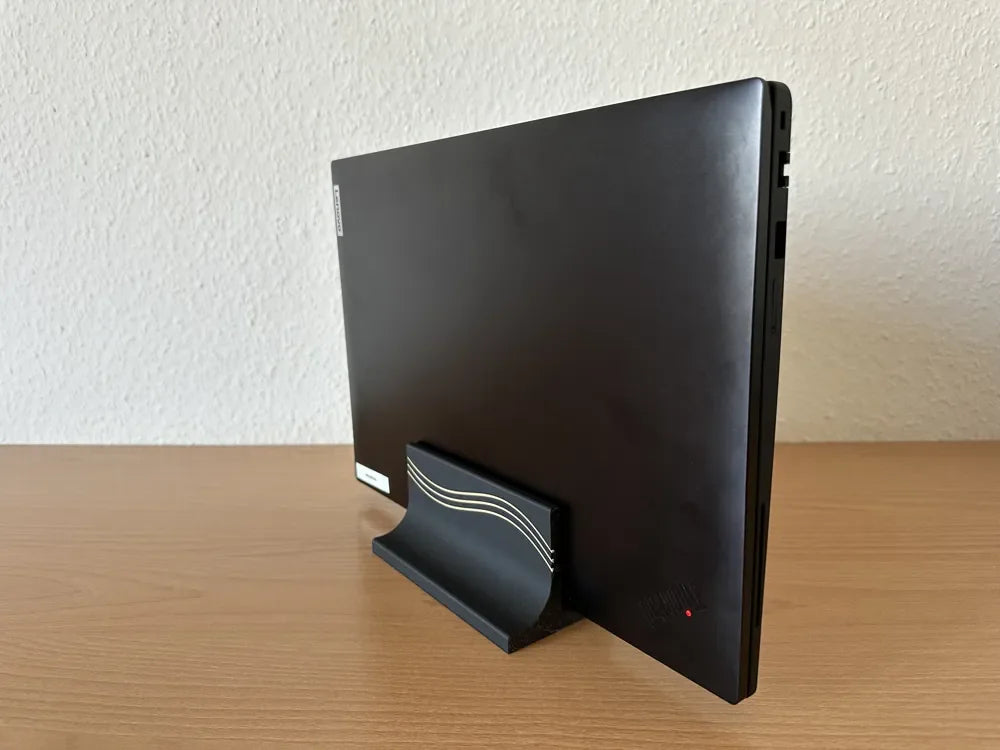 3D printed vertical laptop stand in black holding a closed laptop, side angle