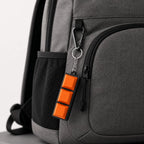 Orange 3-key mechanical fidget keychain on a grey backpack