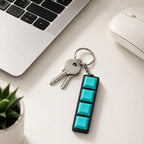 Teal 4-key mechanical keychain with house keys beside a laptop